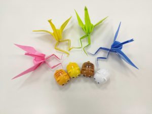 ピンク、黄色、黄緑、青の足の生えた折り鶴と、コロッと丸い動物のマスコットが並んでいる。